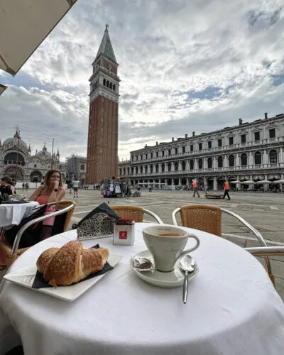 Coffee and croissant on café table in St Mark’s Square with St Mark’s Campanile in Venice Italy
