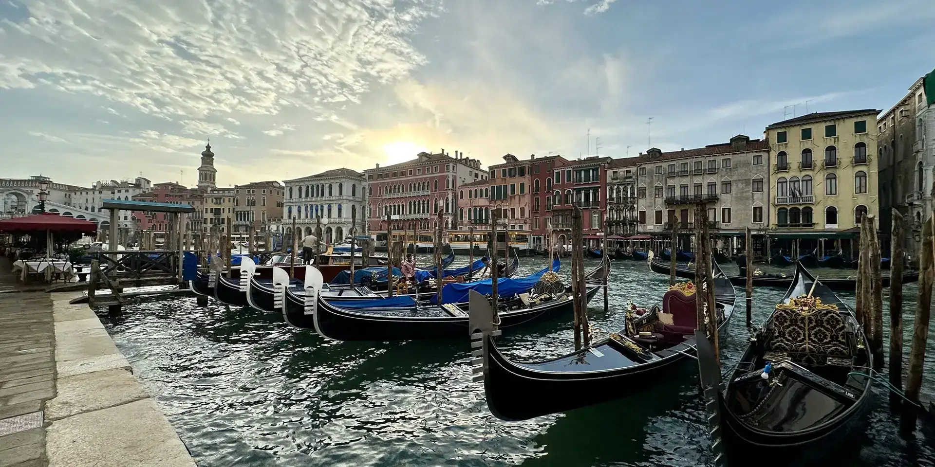 Gondolas moored along a canal in Venice with historic buildings and soft evening light reflecting on the water.