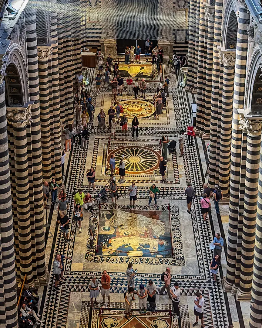 Inlaid marble floor of the Duomo di Siena seen from above between the cathedral’s striped columns