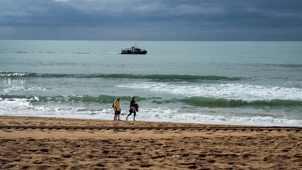 Deux personnes marchant sur une plage peu fréquentée de l’Algarve sous un ciel hivernal nuageux.