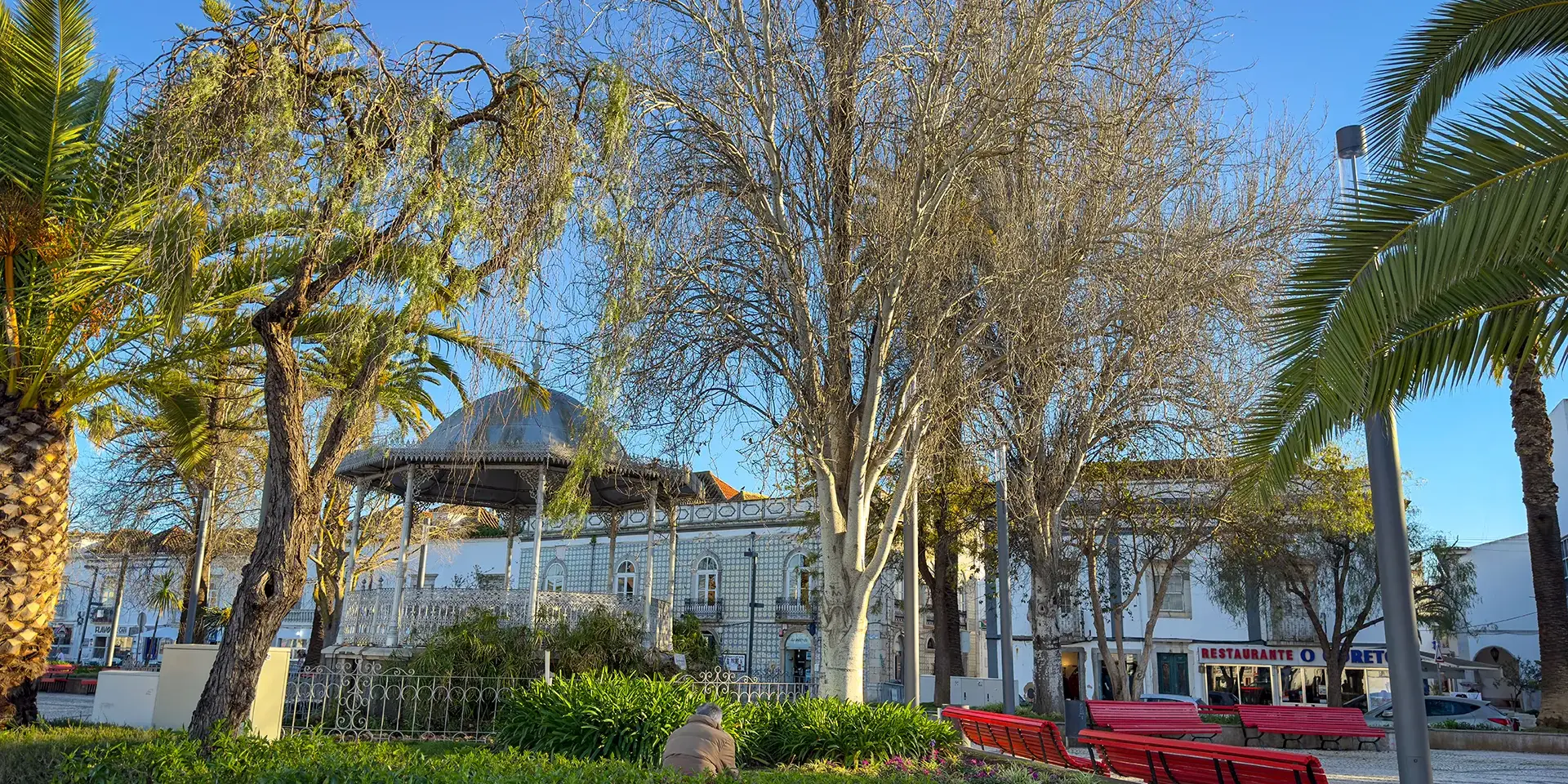 Parc public à Tavira avec bancs, arbres et soleil hivernal de l’Algarve.