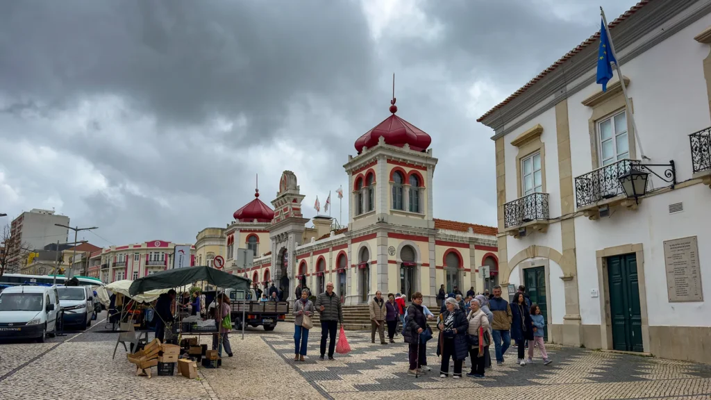 People shopping and walking outside Mercado de Loulé on a Saturday market day with street stalls, calçada pavement, and cloudy winter skies.