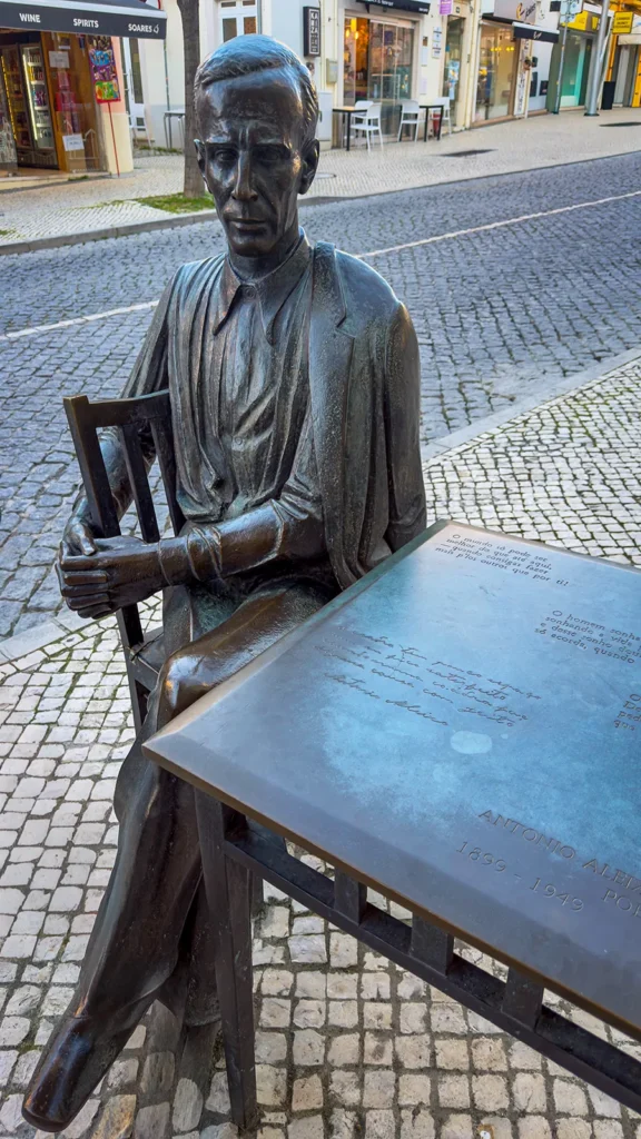 Bronze statue of António Aleixo seated at a table with engraved poetry in Loulé, Portugal.