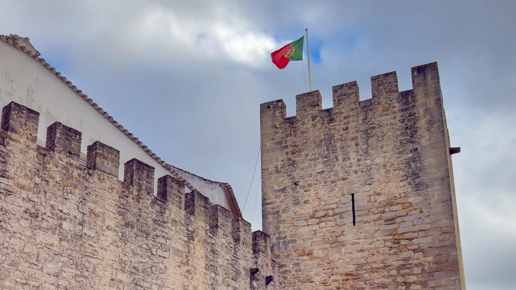 Stone walls and tower of Castelo de Loulé beneath a Portuguese flag in Loulé, Portugal.