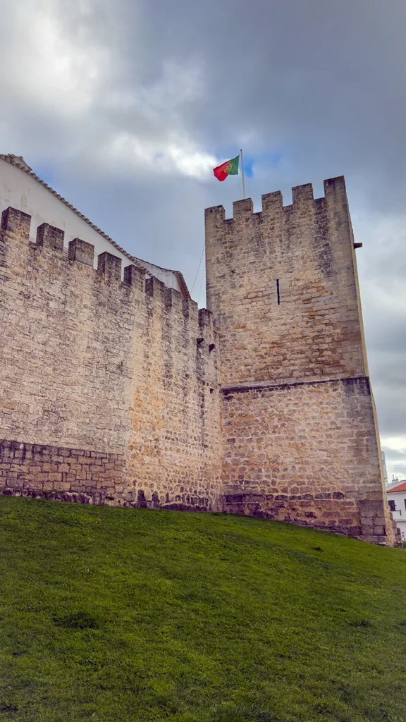 Medieval stone walls and tower of Castelo de Loulé beneath a Portuguese flag and winter clouds in the Algarve.