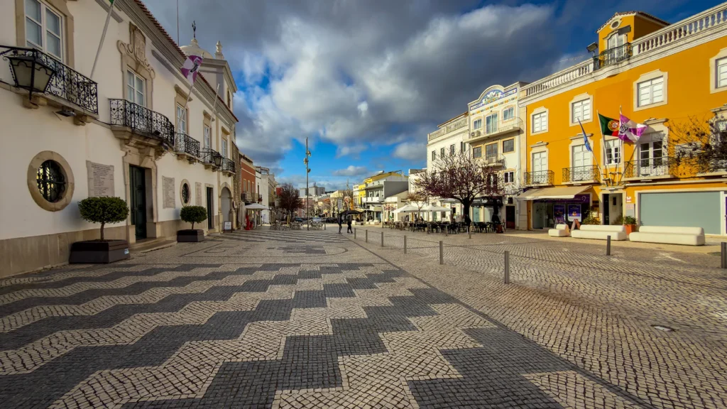 Traditional calçada stone pavement in the historic center of Loulé, Portugal, with colorful buildings and winter clouds overhead.