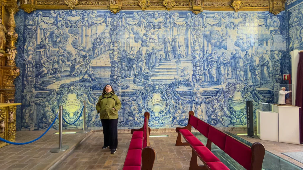 Visitor admiring a large blue-and-white azulejo tile mural inside Ermida de Nossa Senhora da Conceição in Loulé, Portugal.