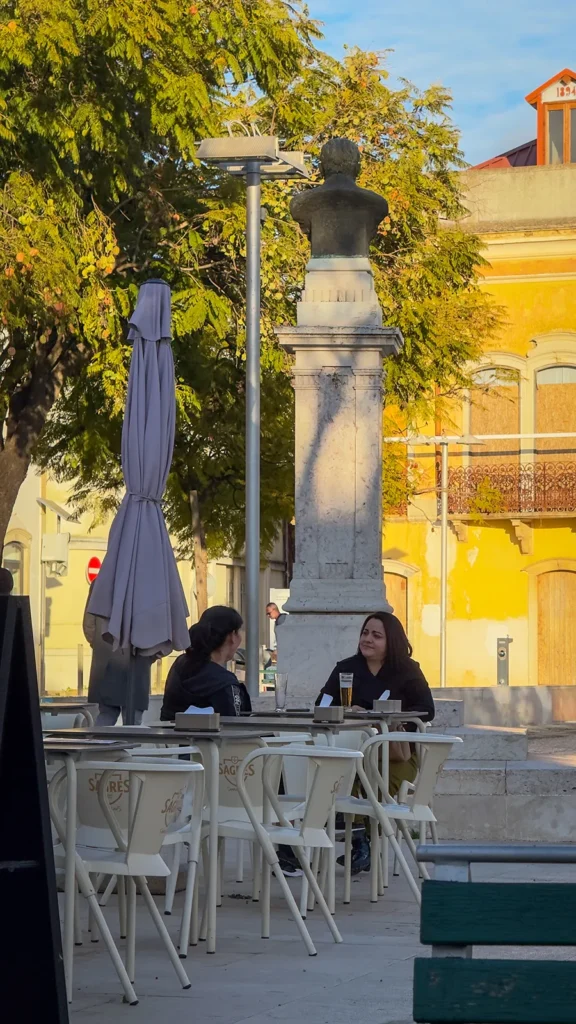 Two women seated at an outdoor café beside a monument and historic buildings in Loulé, Portugal.