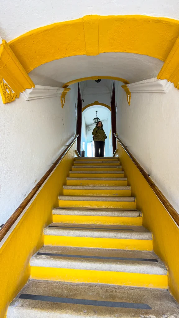 Steep yellow-and-white staircase inside a historic building in Loulé, Portugal, with a woman standing at the top.