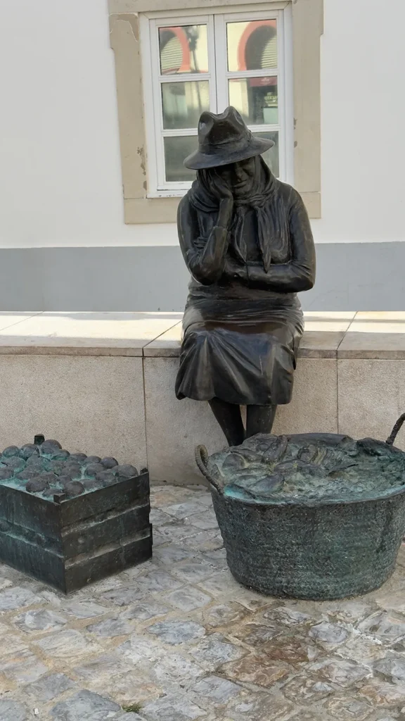 Bronze statue of a seated market woman beside baskets of produce in Loulé, Portugal.