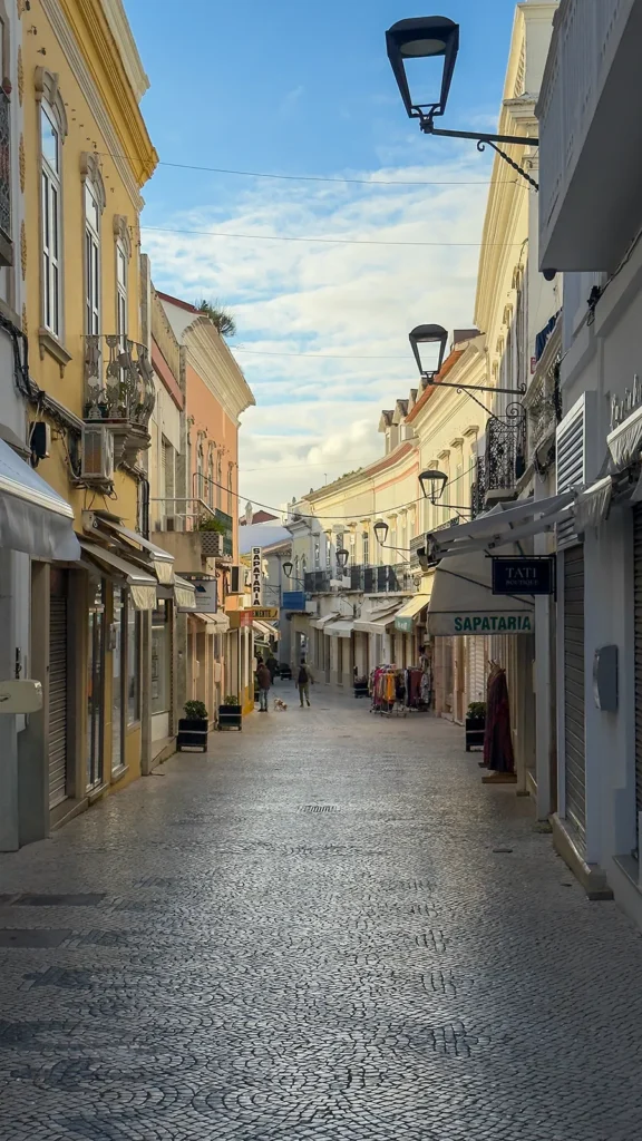 Pedestrian shopping street in Loulé Old Town with small boutiques, traditional buildings, calçada pavement, and a few people walking.