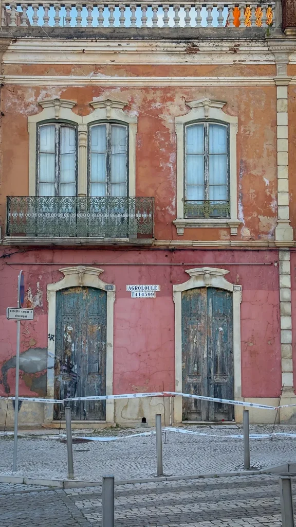 Weathered pink and terracotta building with worn wooden doors and decorative balconies in Loulé Old Town, Portugal.