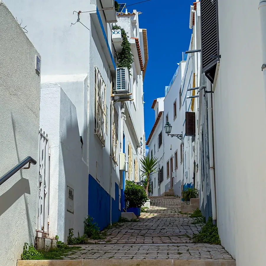 Une ruelle pavée en pente entre des bâtiments blanchis à la chaux dans le centre historique d’Albufeira, au Portugal.