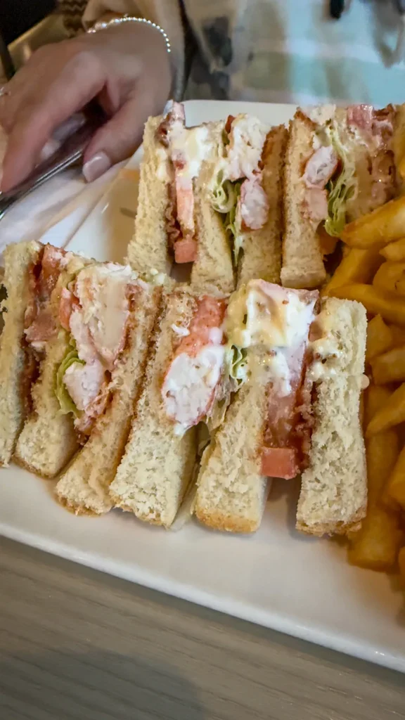Lobster club sandwich cut into quarters on a white plate, with fries alongside.
