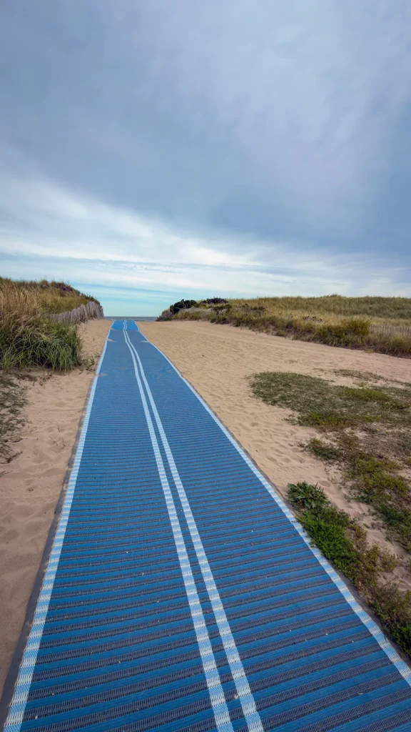 Blue beach access mat laid over sand between grass-covered dunes at Parlee Beach.