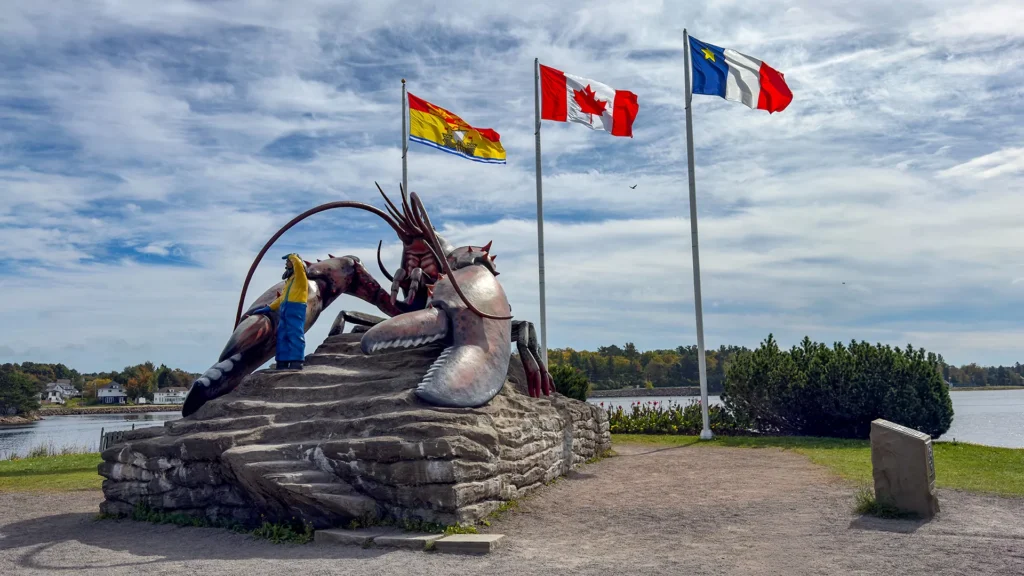Giant lobster sculpture beside the water, with a visitor posing near its claw and three flags flying overhead.