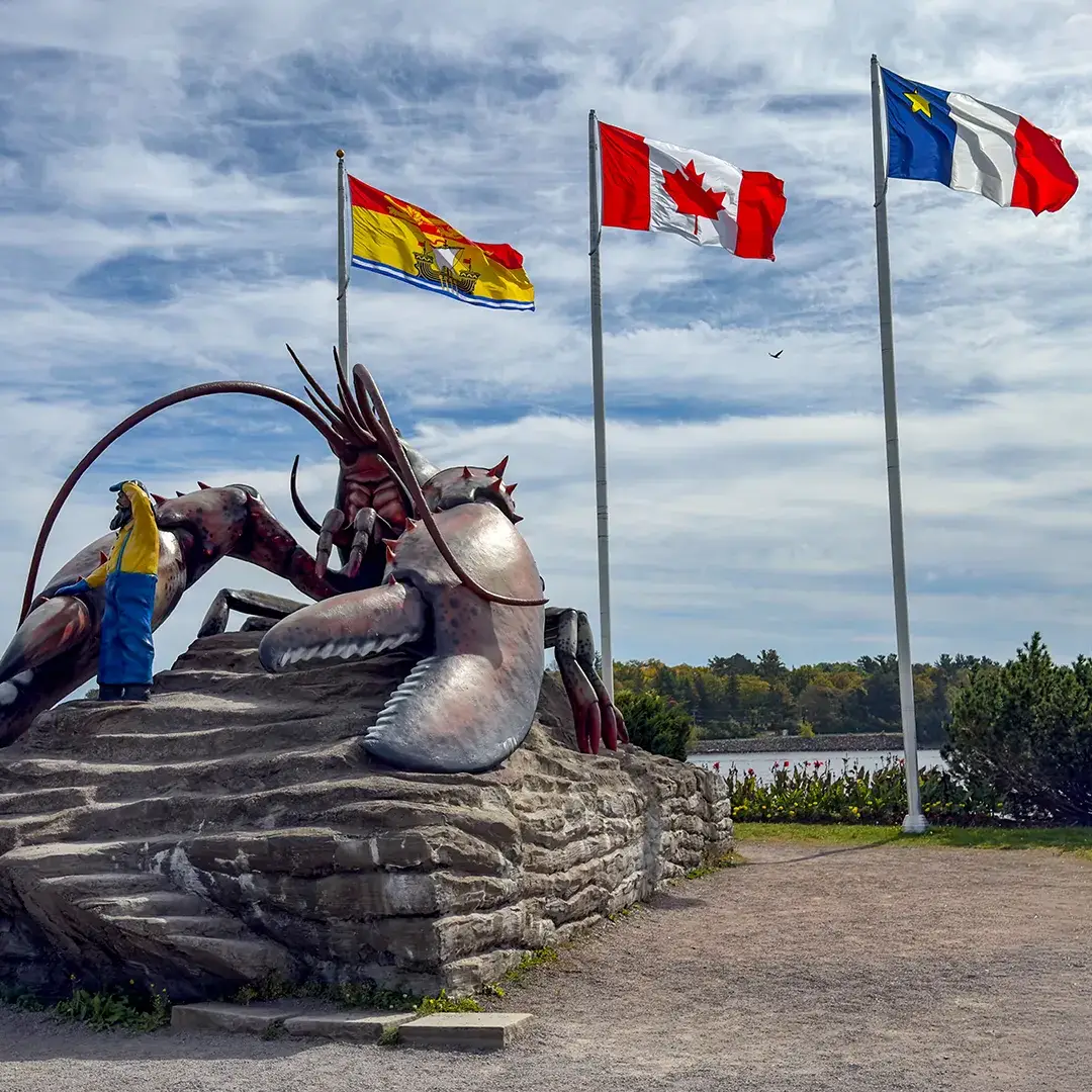 Giant lobster sculpture beside the water, with a visitor posing near its claw and three flags flying overhead.